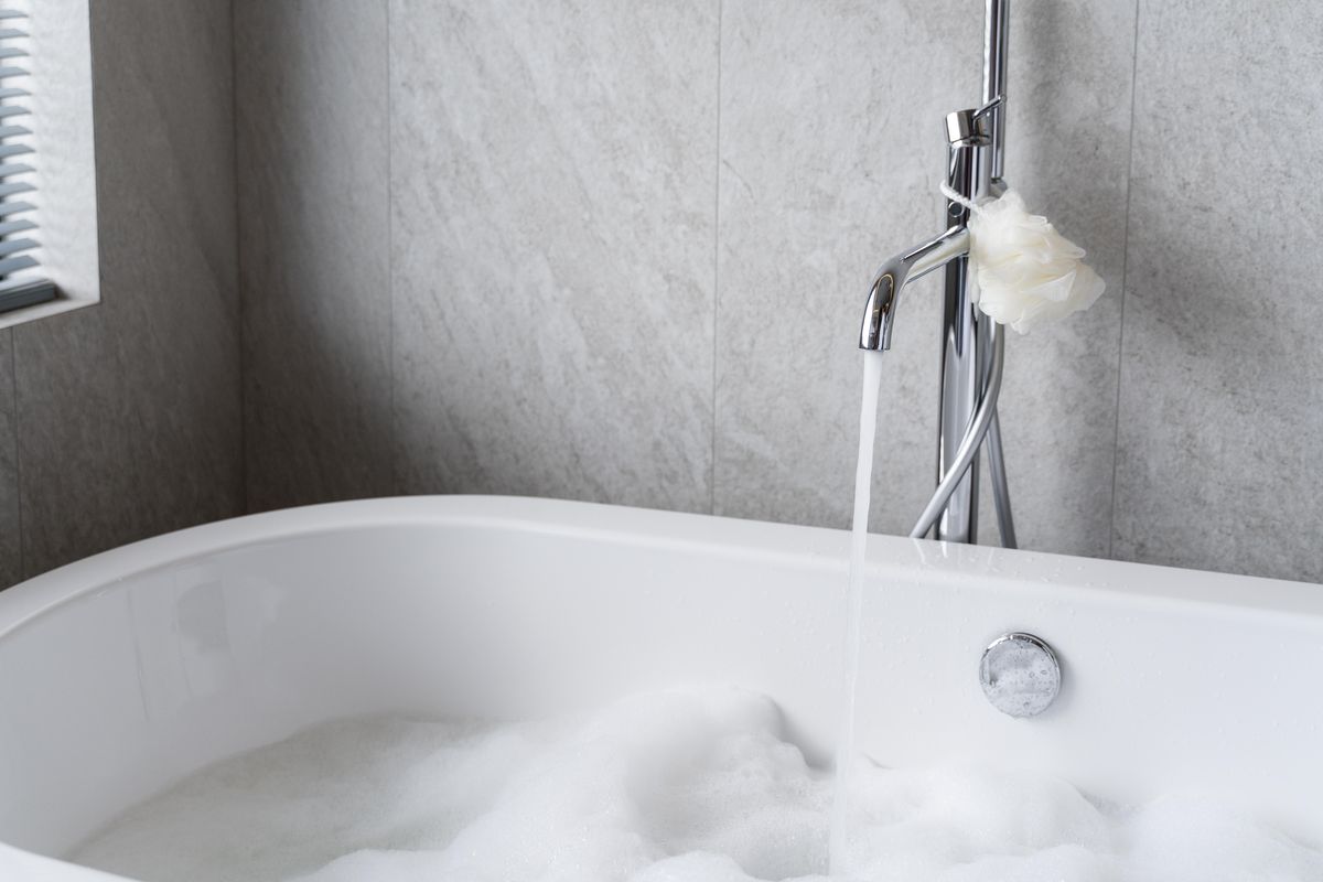 Baignoire blanche en cours de remplissage, avec un robinet chromé sur pied et un trop-plein au-dessus de la mousse.