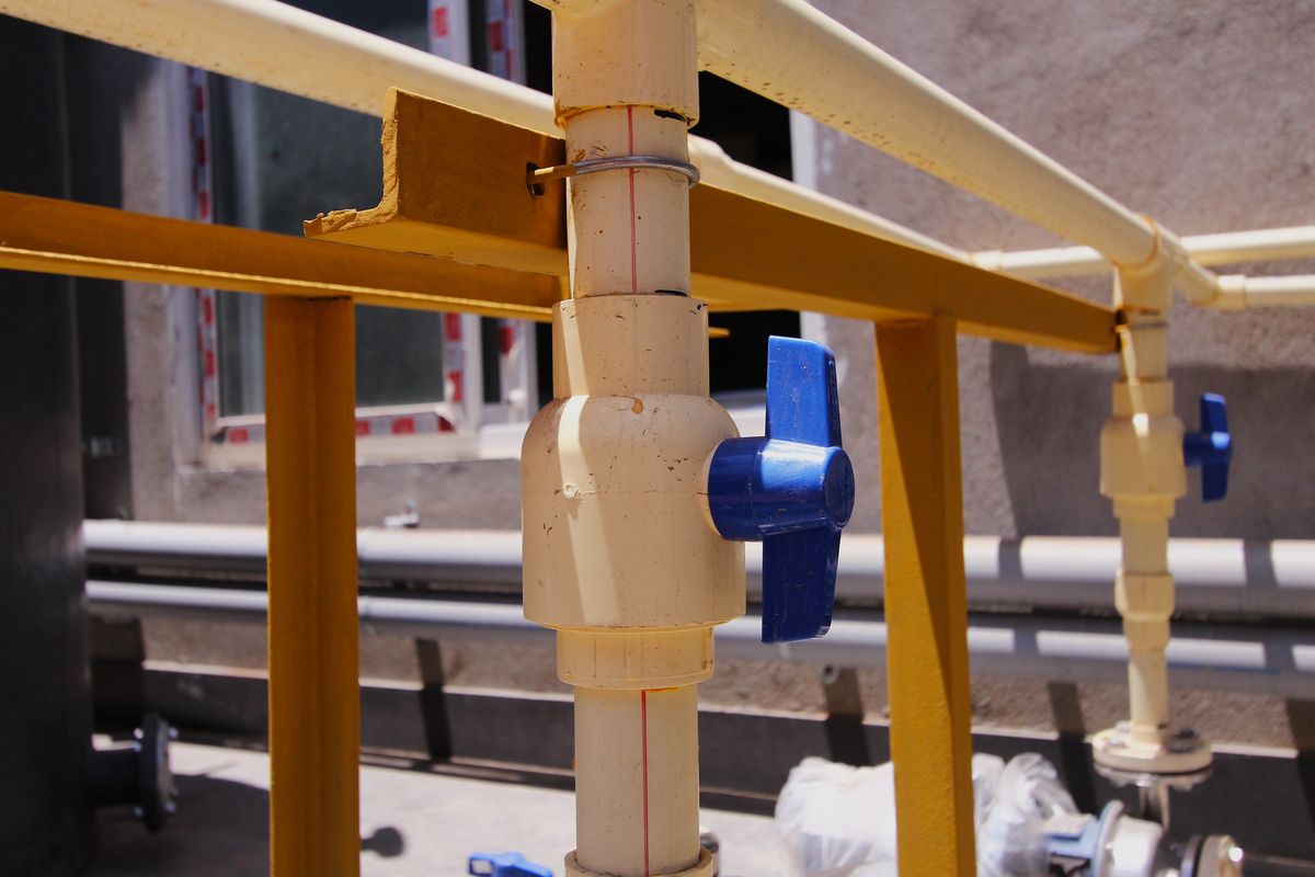 Des canalisations en PVC clair munies de vannes à poignée bleue sont fixées sur une structure métallique jaune.