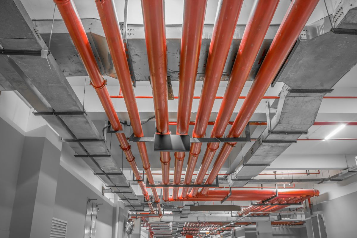 Canalisations rouges et gaines métalliques suspendues sous le plafond en béton d'un sous-sol.