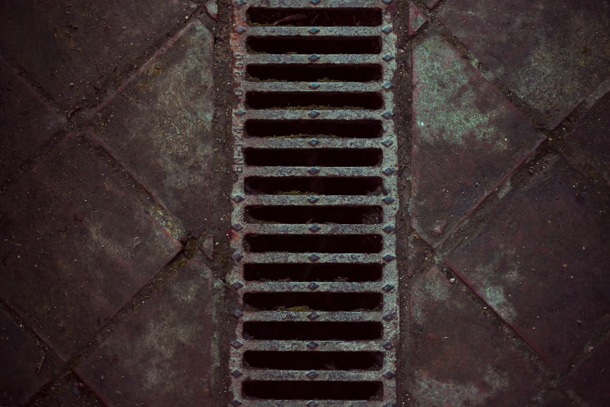 Caniveau à grille métallique encastré dans un sol de dalles sombres et usées.