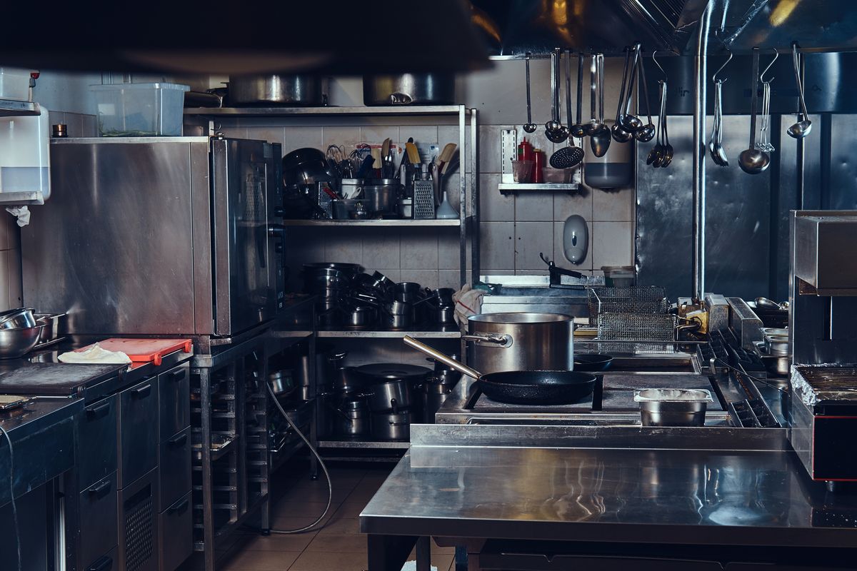 Cuisine professionnelle en inox avec plans de travail, piano et ustensiles suspendus