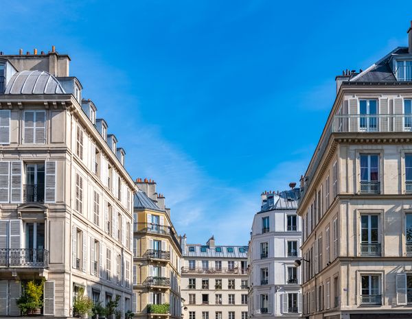 Façades d'immeubles parisiens en pierre de taille, balcons filants et toits en zinc, sous un ciel bleu