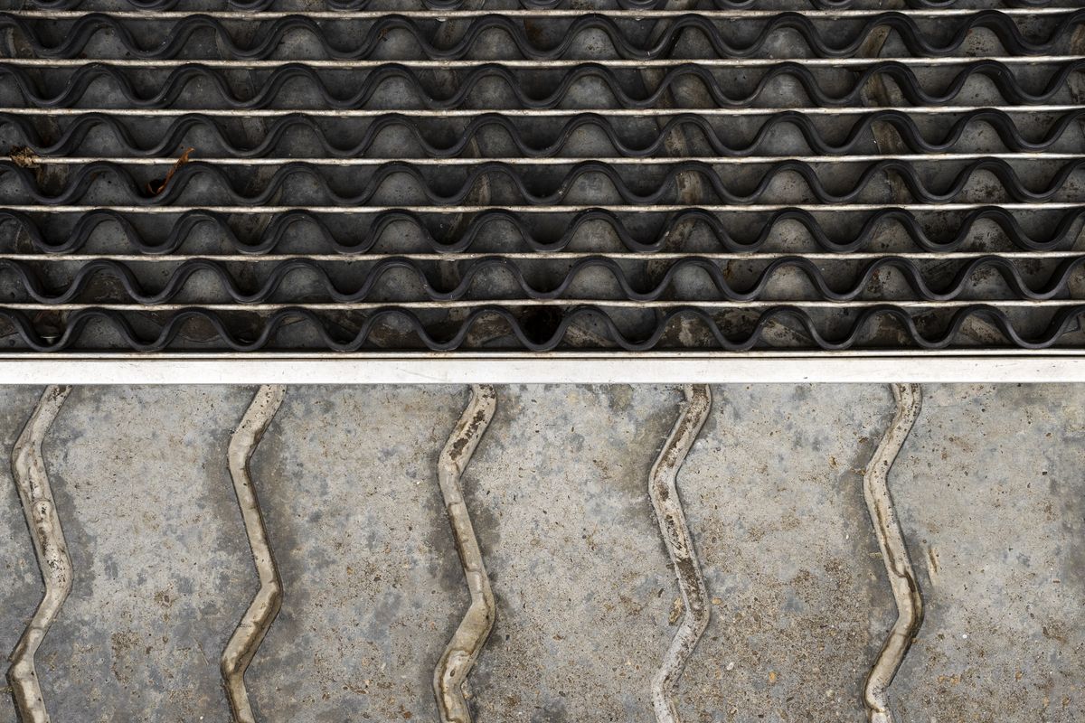 Grille métallique ondulée de caniveau bordant une dalle de pierre grise striée de joints en zigzag.