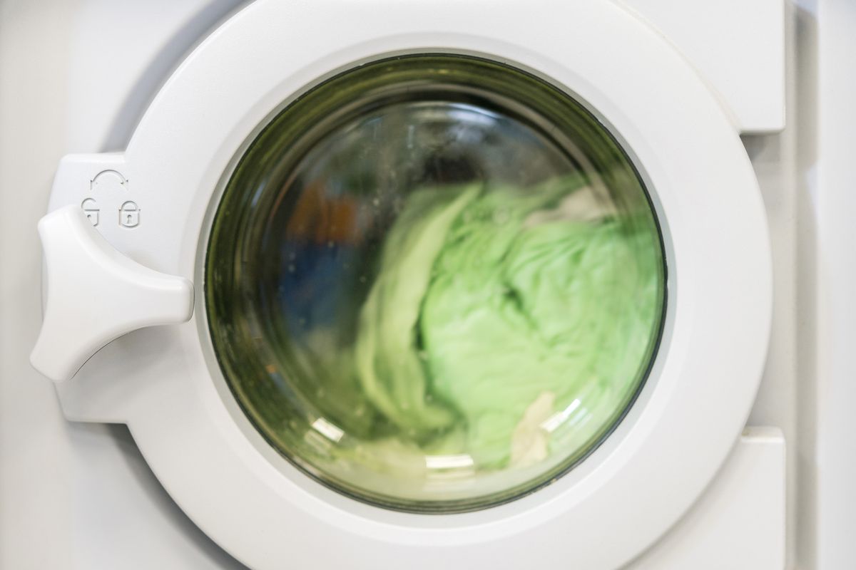 Hublot d'un lave-linge blanc en cours de lavage, avec du linge vert qui tourne dans le tambour.