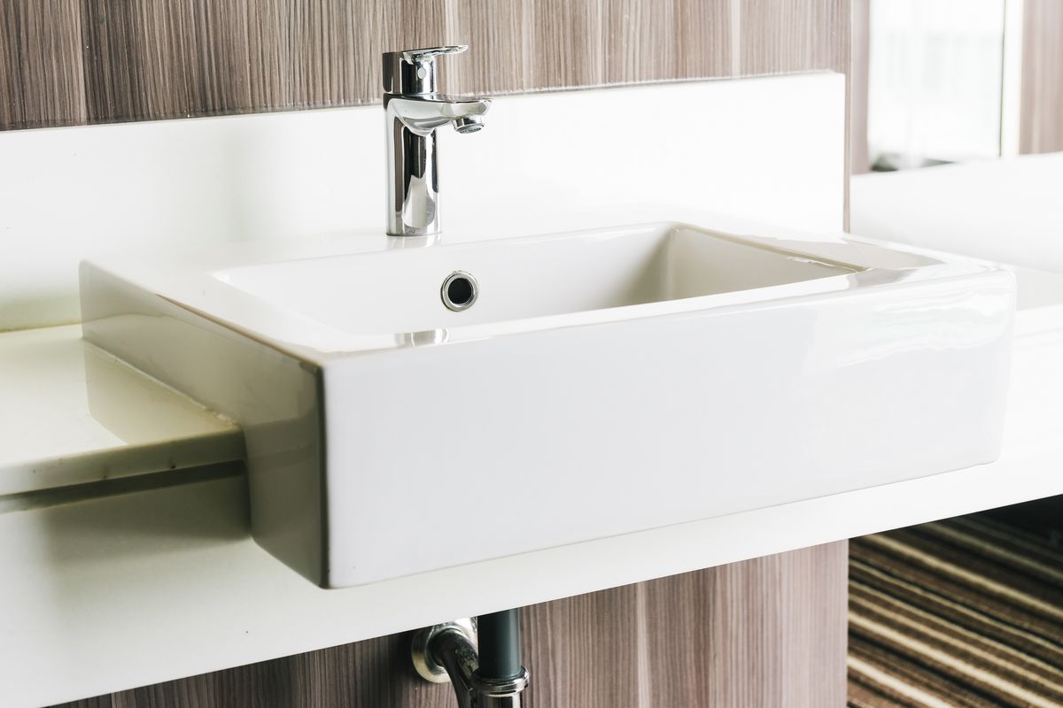 Lavabo rectangulaire blanc posé sur un plan, avec le siphon chromé visible sous la vasque.
