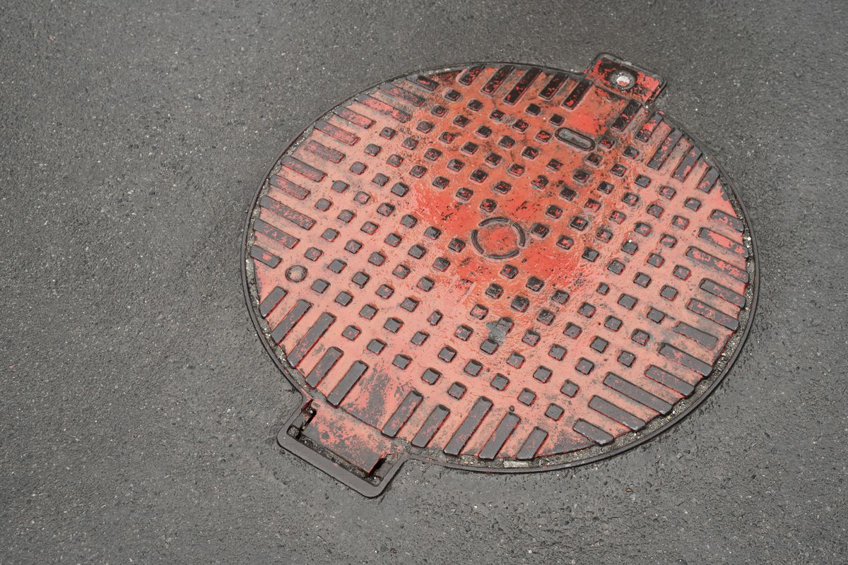 Plaque de regard en fonte rouge sur l'enrobé d'une chaussée, vue de dessus
