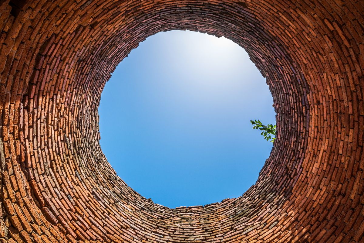 Un puits circulaire en briques est vu depuis le fond, avec un disque de ciel bleu à son ouverture.