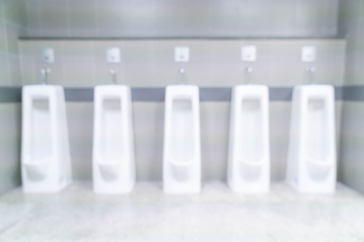 Rangée de cinq urinoirs blancs en céramique fixés au mur de sanitaires collectifs, dans une image légèrement floue.