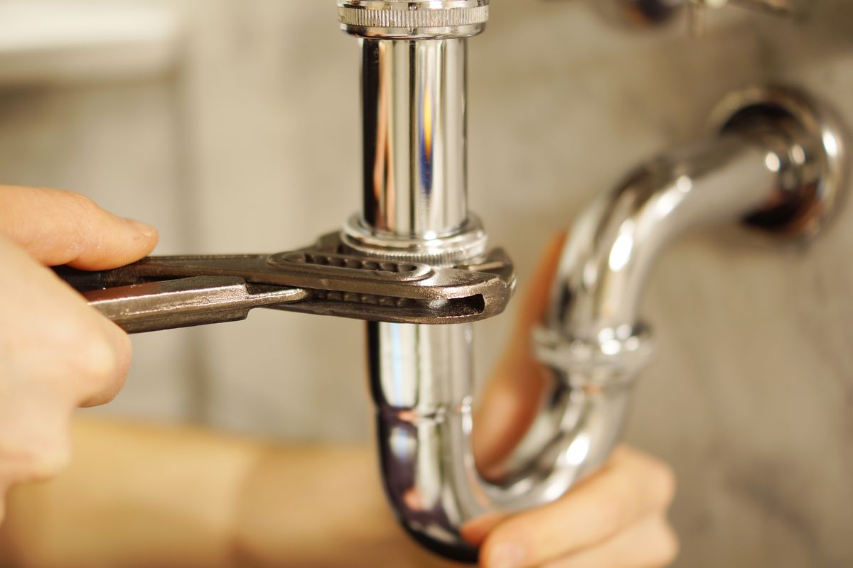 Deux mains démontant un siphon chromé à la clé à molette