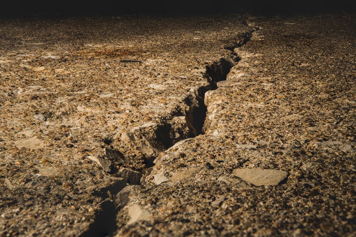 Sol de terre sèche et caillouteuse fendu par une longue fissure, éclairé par une lumière rasante.