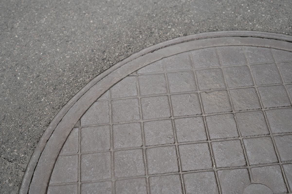 Tampon de regard métallique rond, à motif quadrillé, posé dans une surface en asphalte gris.