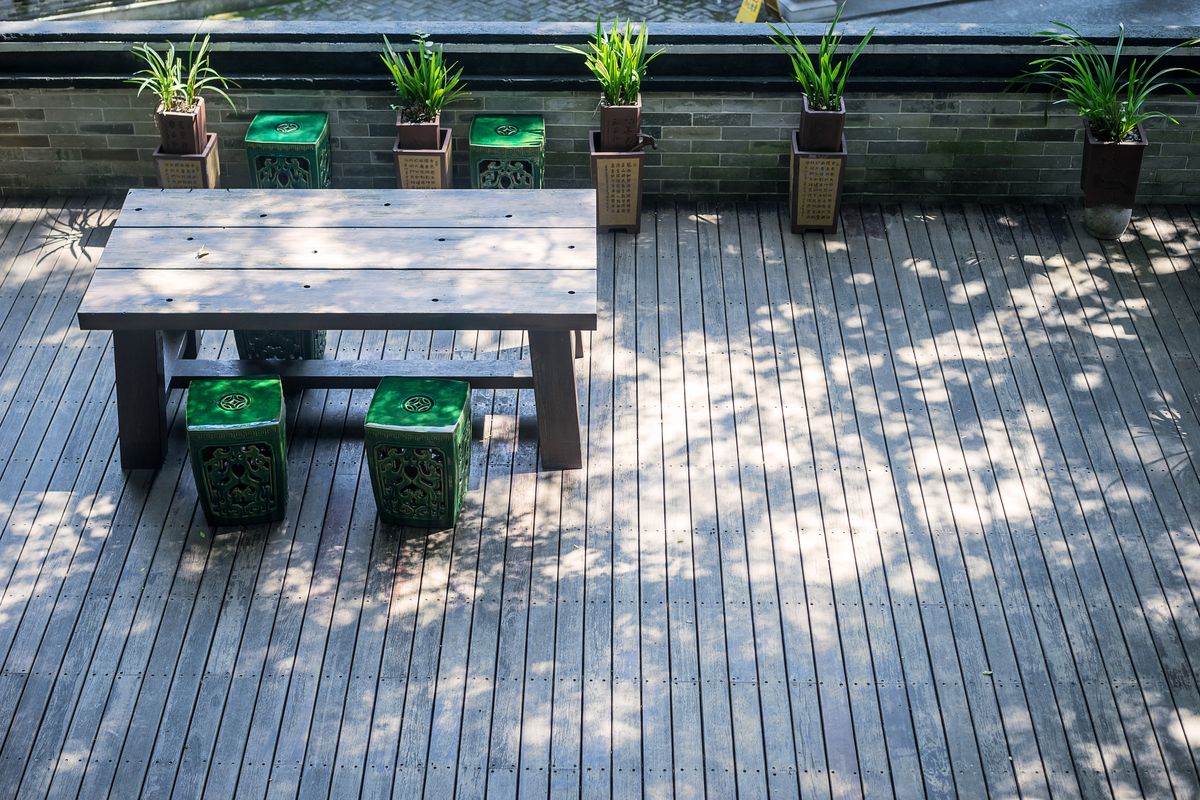 Terrasse en toit au platelage de bois gris, avec une table, des tabourets verts et des plantes en pot.