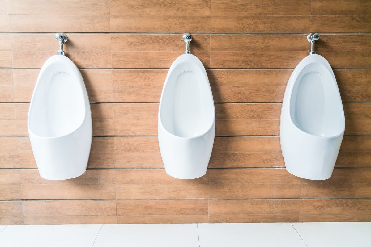 Trois urinoirs blancs en céramique sont fixés côte à côte sur un mur habillé de lames de bois.