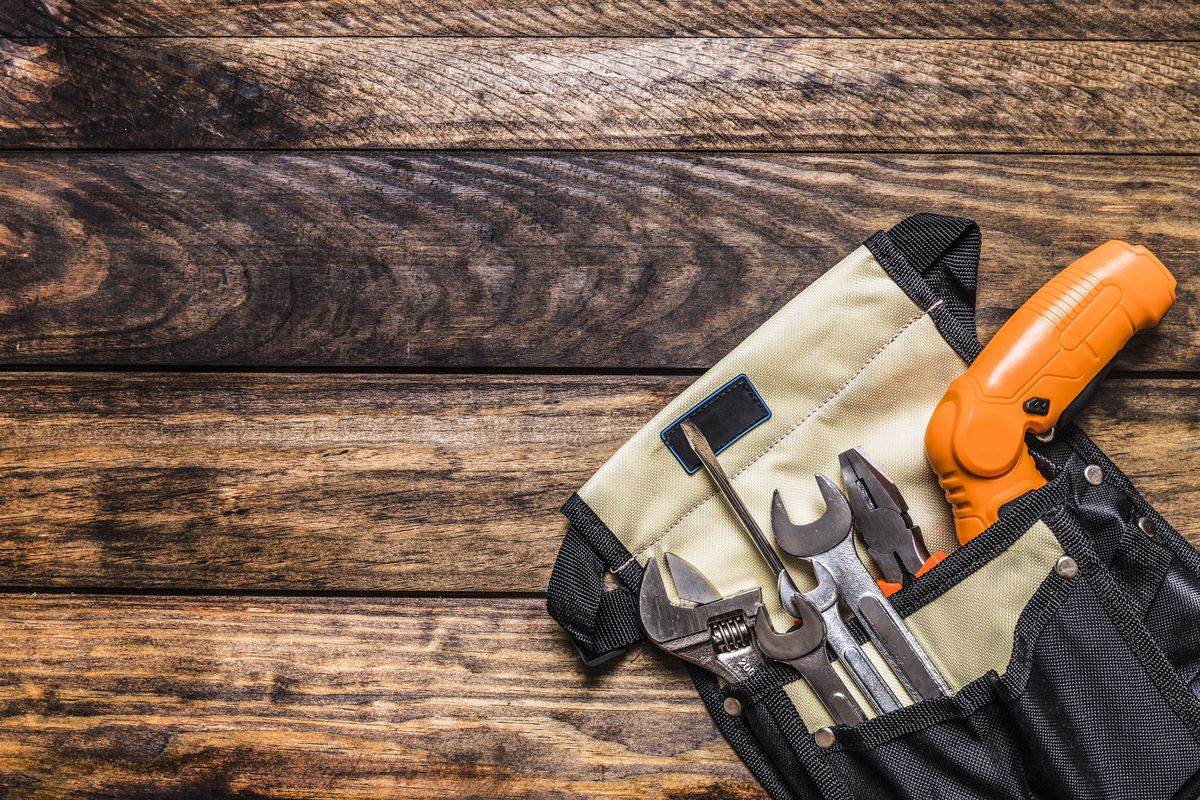 Trousse à outils en toile ouverte sur un plancher, garnie de clés, d'une pince et d'un tournevis.
